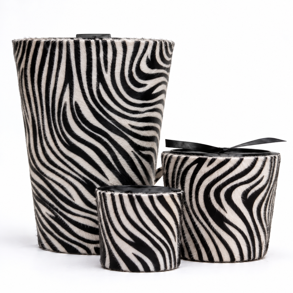 Three zebra-print fuzzy cylindrical containers or candle holders with black ribbon accents, arranged on a white background.