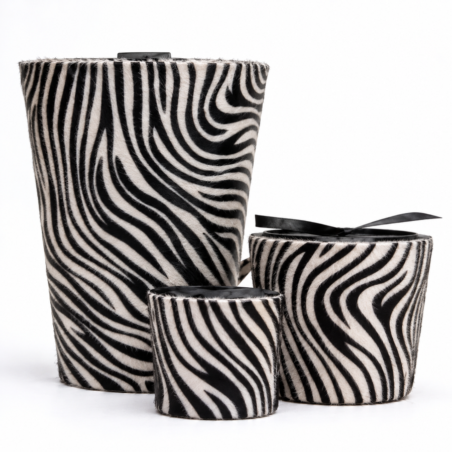 Three zebra-print fuzzy cylindrical containers or candle holders with black ribbon accents, arranged on a white background.